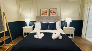 A neatly made bed with a dark blue bedspread and white pillows, two bedside tables with lamps, a hanging light fixture, and two framed pictures on the wall. - Euro Bar and Hotel (Oxford)