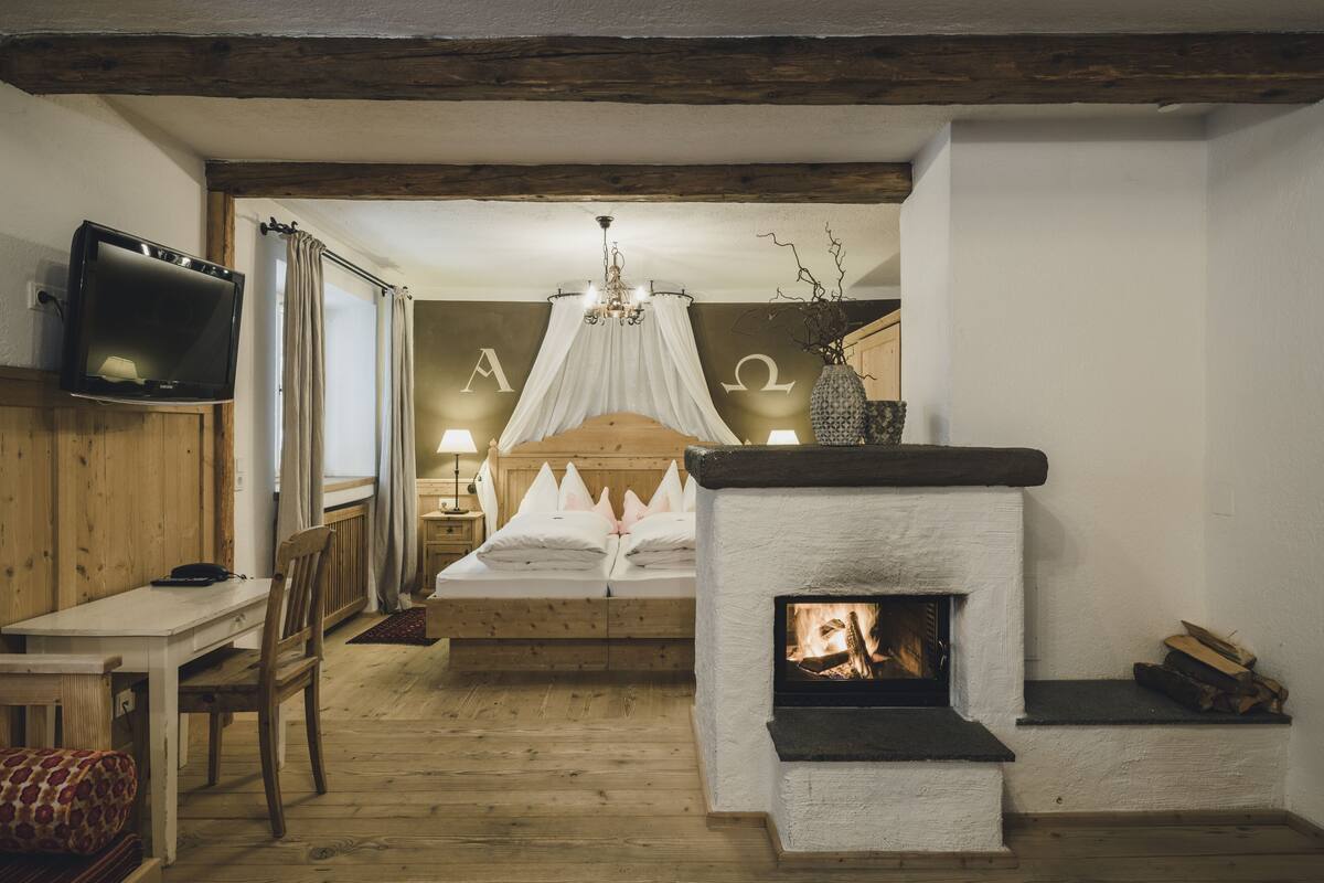 A cozy bedroom with a wooden bed, a television, a fireplace, and a nightstand with a lamp.