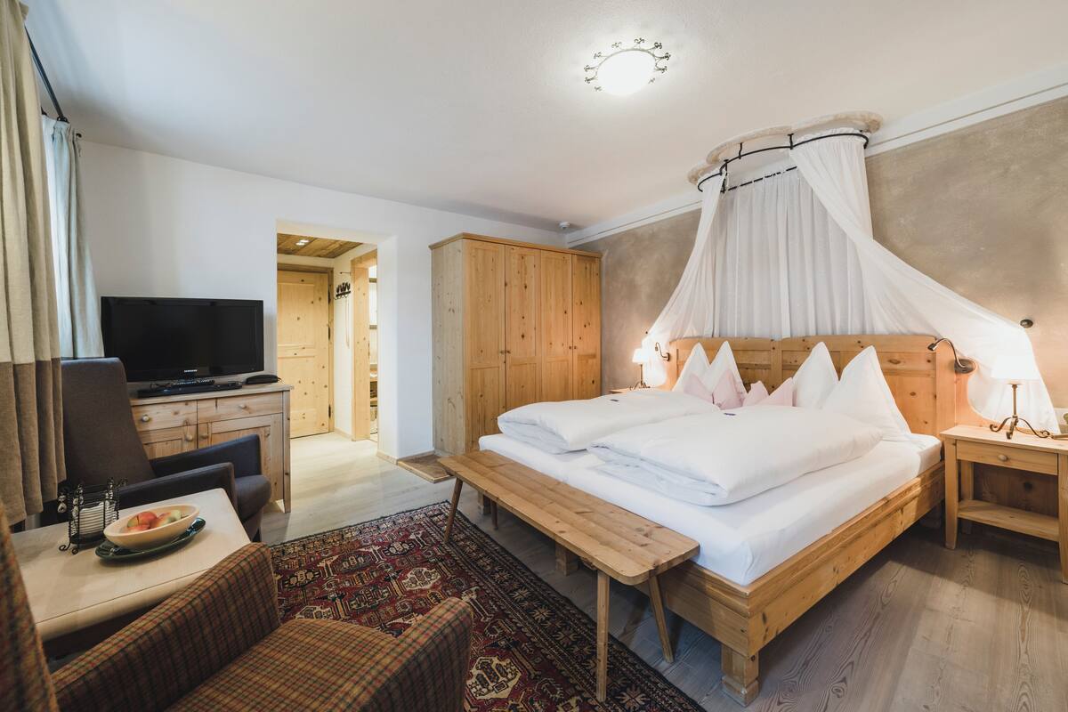 A hotel room with a wooden bed, a TV, a desk with a bowl of fruit, and a patterned rug.