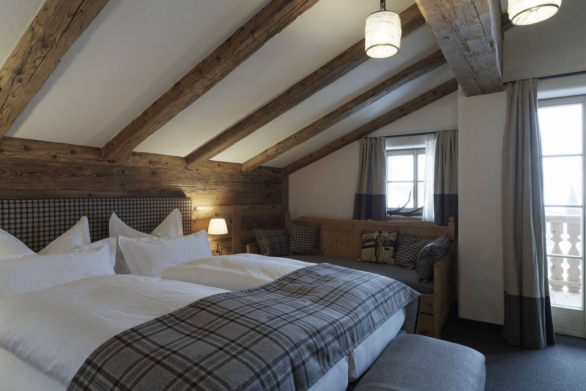 A bedroom with a large bed, a wooden headboard, a bench, and a window with curtains.