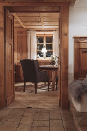 A wooden interior with a dining area, a chair, a table with a lamp, and a window with curtains. - Himmlhof (Sankt Anton am Arlberg)