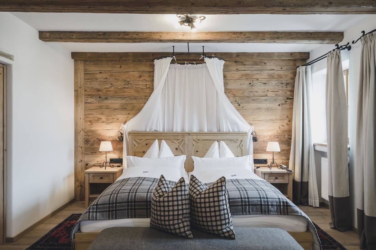 A bedroom with a wooden headboard, two bedside tables with lamps, a canopy bed, and plaid bedding.