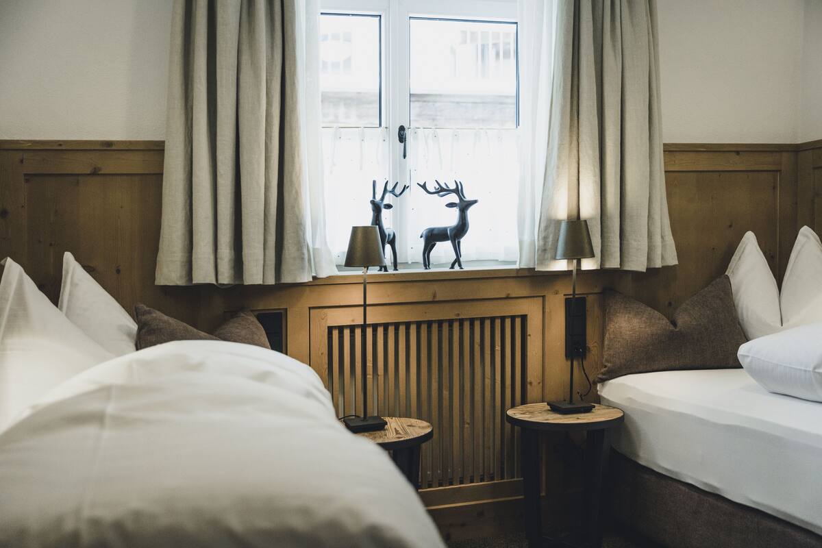 A hotel room with two beds, a window with curtains, a lamp, and a small table.