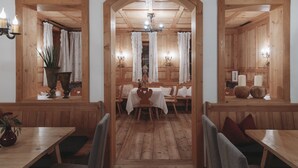 Un interno in legno con un tavolo centrale e panche, affiancato da finestre con tende e lampade a parete.
