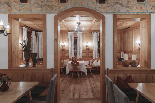 A wooden interior with a central table and benches, flanked by windows with curtains, and wall-mounted lamps. - Himmlhof (Sankt Anton am Arlberg)