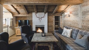 Una camera accogliente con camino, travi in legno, un divano, un tavolo con una candela e un televisore.