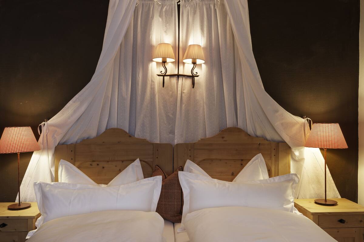 A double bed with white linens, two bedside tables with lamps, and a canopy over the bed.