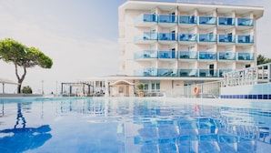 Ett modernt hotell med en swimmingpool, flera balkonger och en klar himmel.