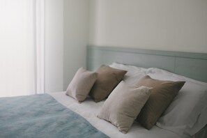 Una cama con una manta azul claro y tres almohadas color beige.