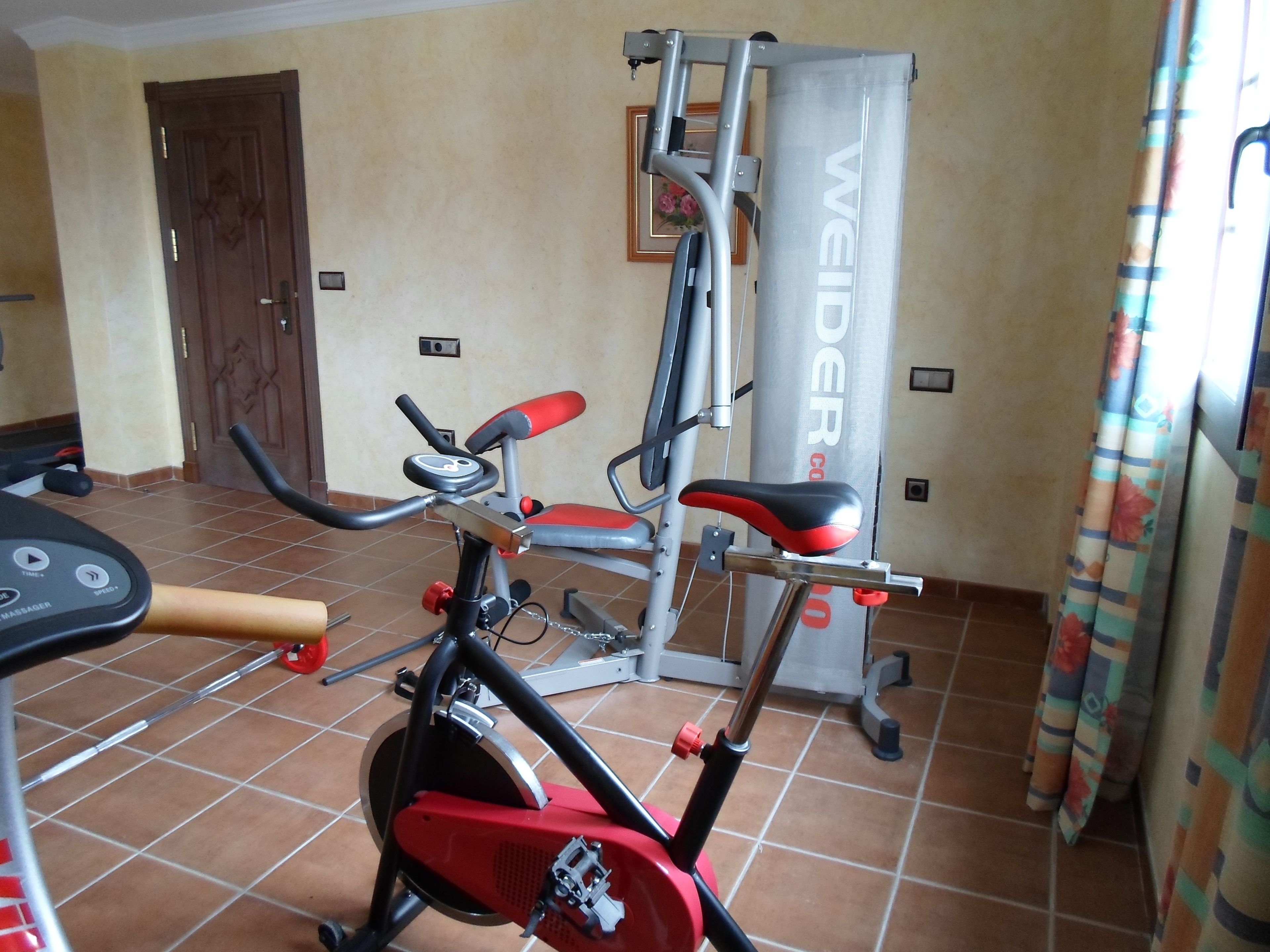 Un gimnasio en casa con una bicicleta estática, una cinta de correr y una máquina de pesas.