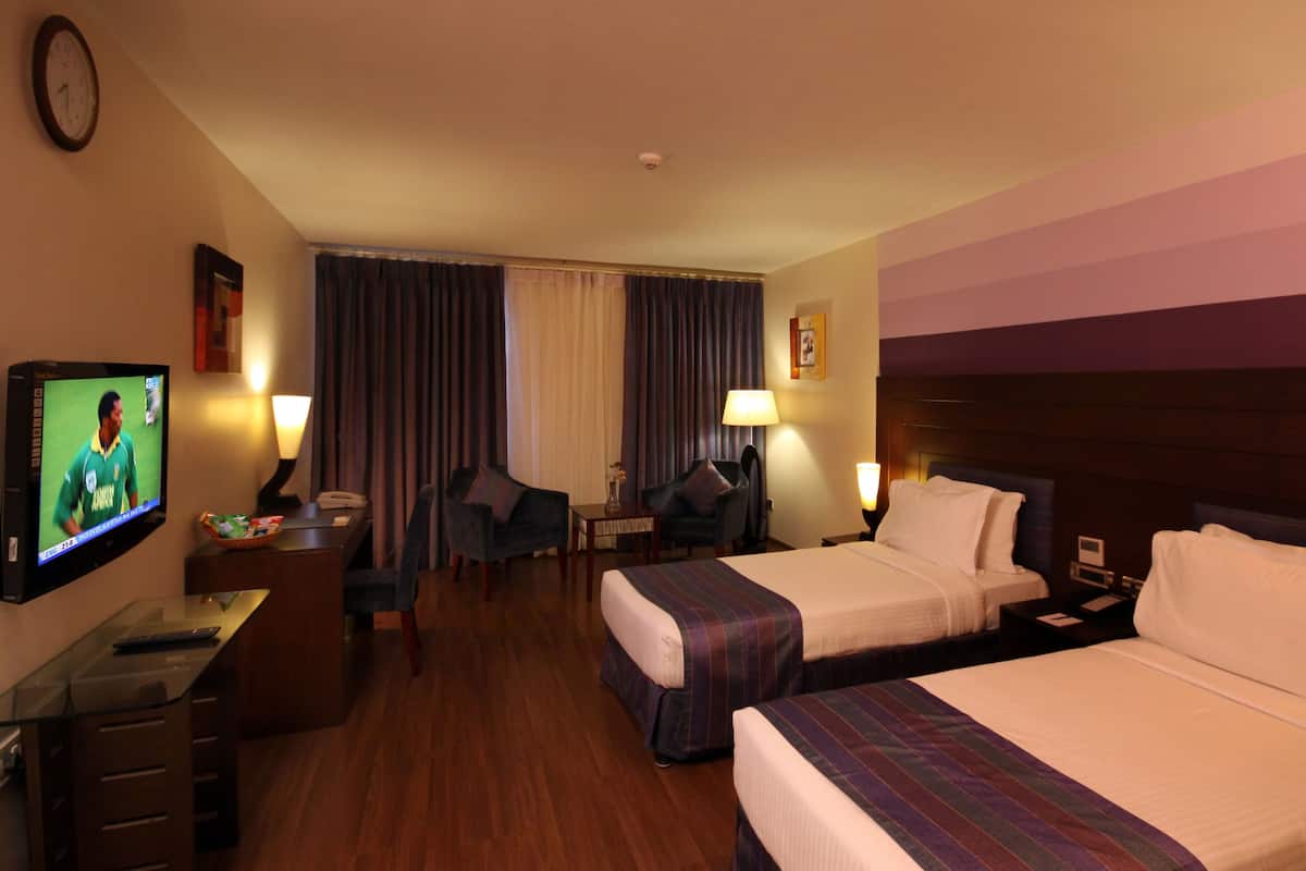 Habitación de hotel con dos camas, un escritorio con computadora, televisor y una silla.