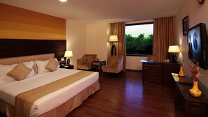 Habitación de hotel con una cama grande, dos sillones, un escritorio y un televisor.
