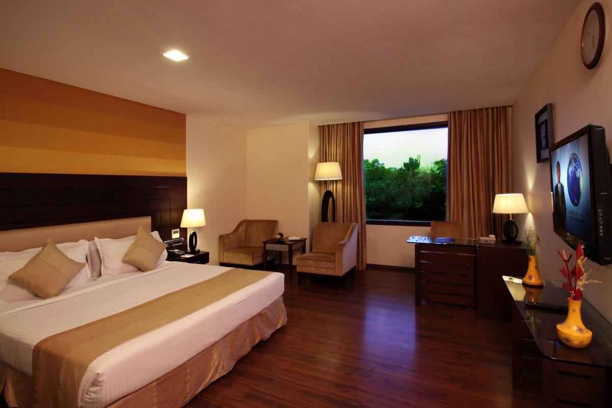 Habitación de hotel con una cama grande, dos sillones, un escritorio y un televisor.