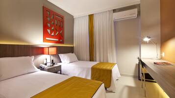 Een hotelkamer met twee bedden, een bureau, een lamp, een airconditioner en een decoratief wandobject.