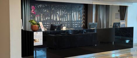 En moderne reception med bordplade i sort marmor, en potteplante og en dekorativ skærm med palmeblade.