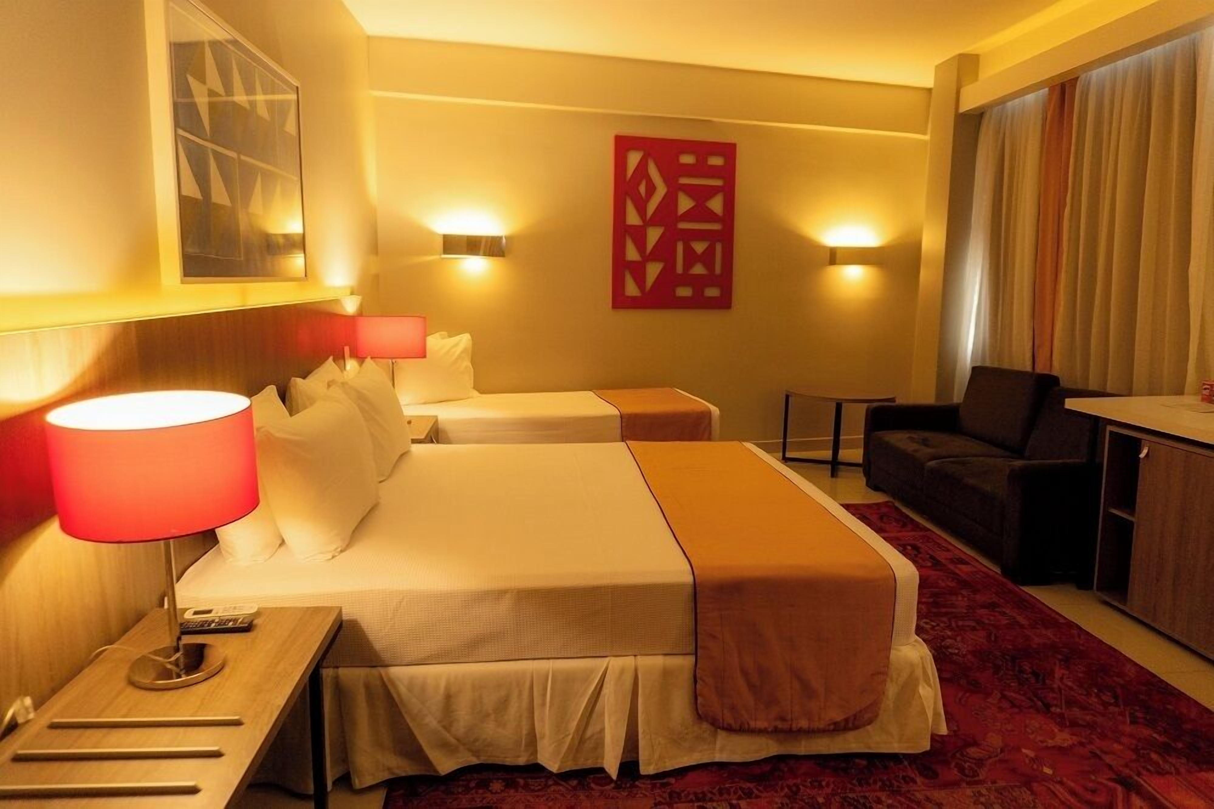 A hotel room with two beds, a desk, a chair, a red decorative wall piece, and a red carpet.