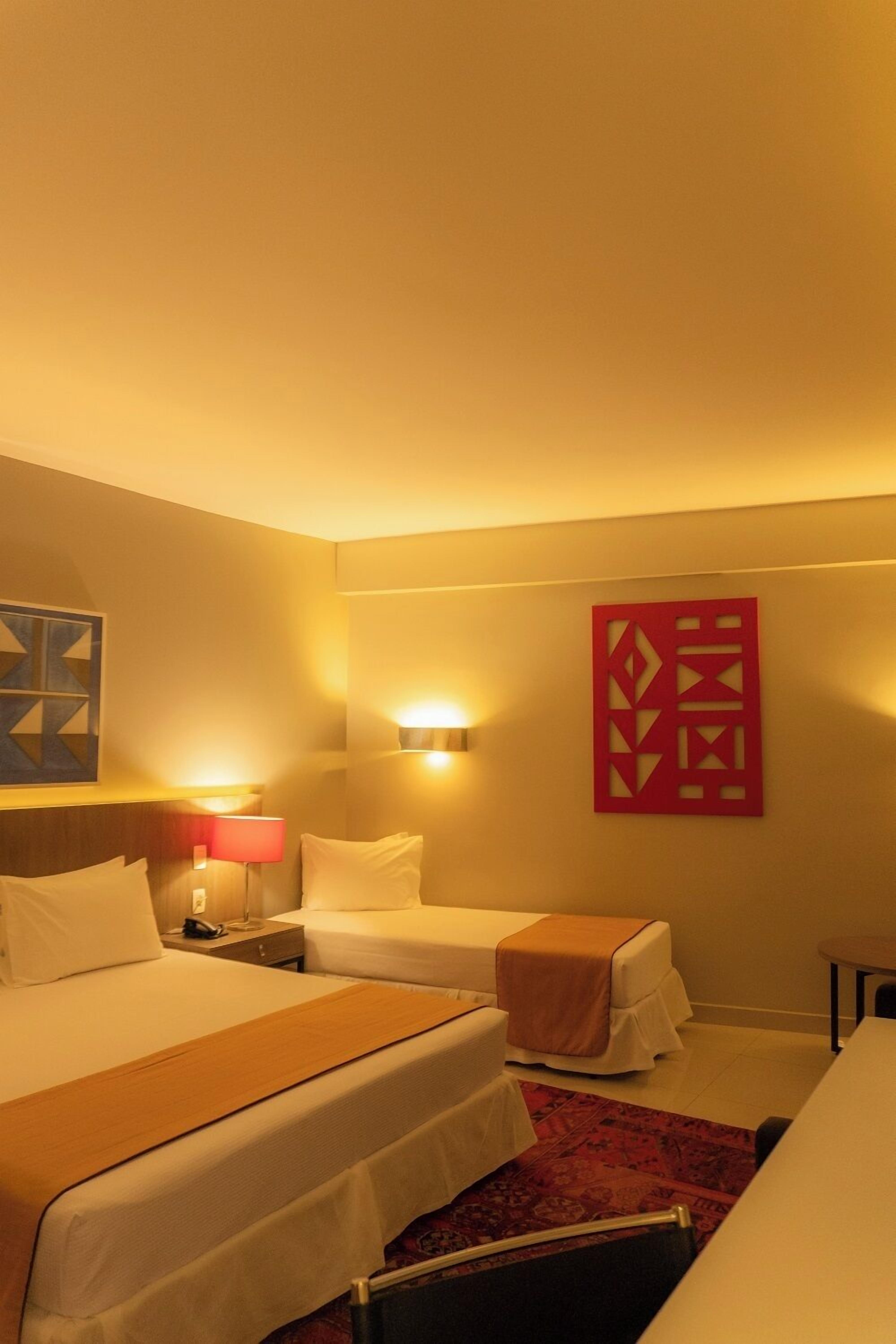 Habitación de hotel con dos camas, una mesita, una lámpara de pared y un adorno mural.