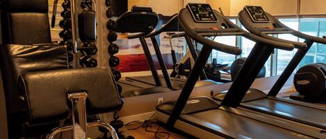 Un gimnasio con cintas de correr, máquinas de pesas y un espejo.