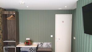 A compact room with a small table, two blue stools, a wooden wardrobe, a white door, and a wall-mounted TV. - Hotel Old Nickel (Amsterdam)