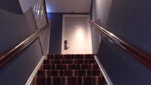 A staircase with a striped carpet, white handrails, and a door at the top. - Hotel Old Nickel (Amsterdam)