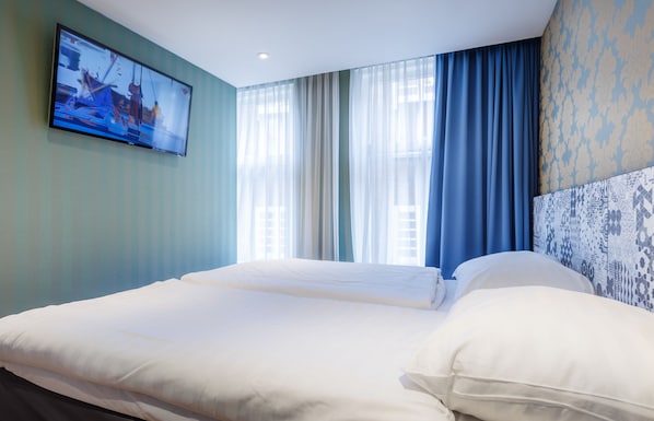 Une chambre d’hôtel avec un grand lit, un téléviseur à écran plat fixé au mur et une fenêtre ornée de rideaux légers.