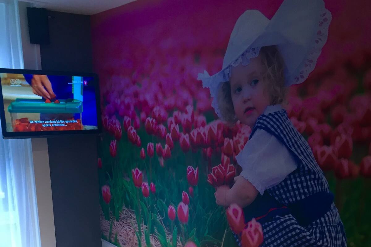 A room with a massage table, a TV on the wall, and a mural of a child with tulips.
