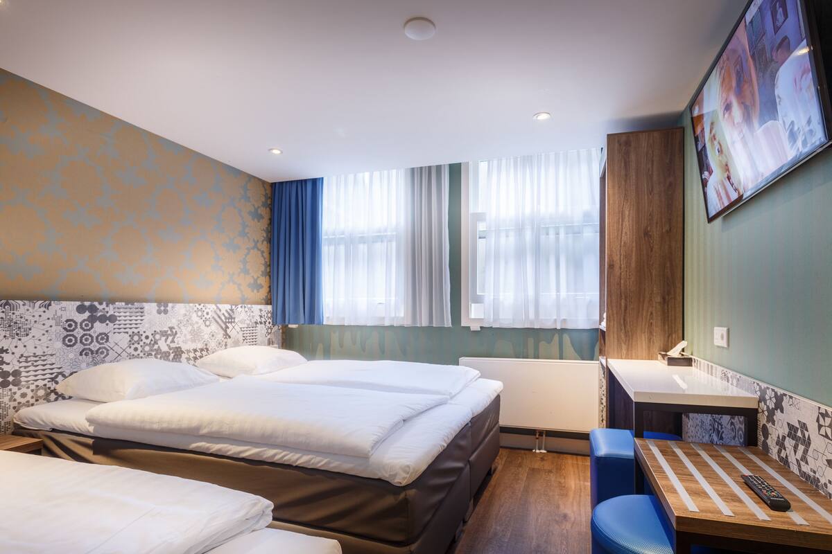 A hotel room with two beds, a desk, a chair, a TV, and a window with curtains.