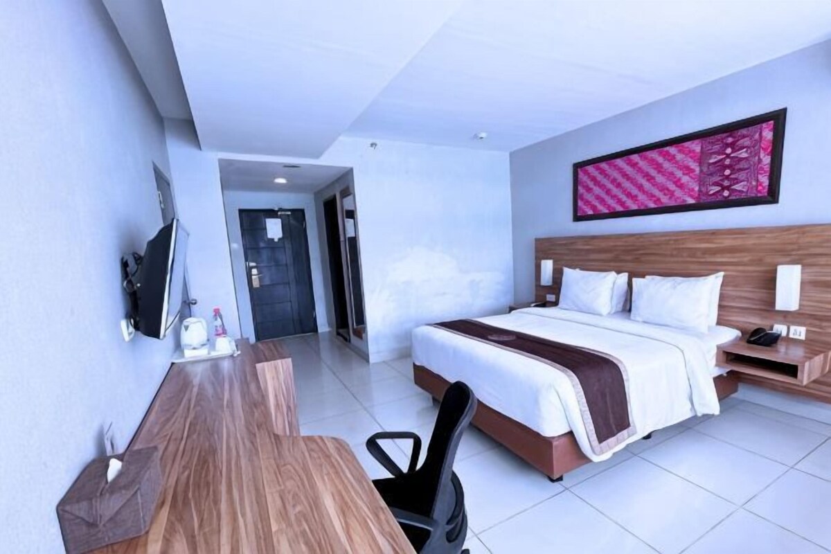 A hotel room with a bed, desk, chair, and a TV.