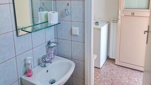 A bathroom with a glass shelf holding toiletries, a sink with a pink soap dispenser, and a mirror above it. - Loukas Pension (Mykonos)