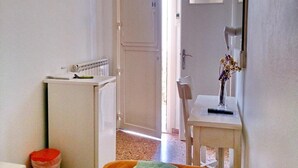 A narrow hallway with a radiator, a white door, and a small table with a vase. - Loukas Pension (Mykonos)