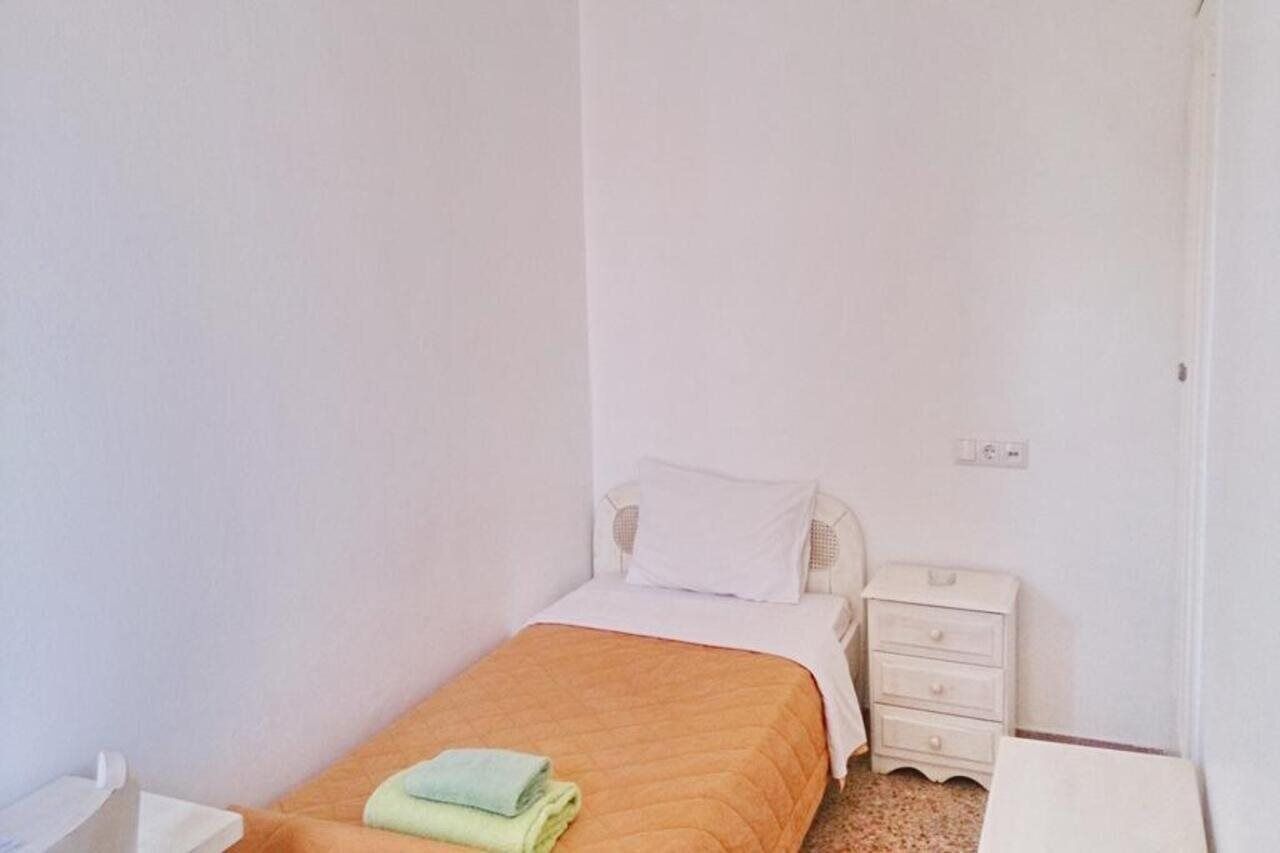 Una habitación pequeña con cama individual, mesita de noche blanca y cómoda blanca.