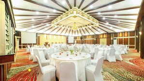 Une salle de banquet avec des tables rondes, des chaises blanches et un tapis à motifs.