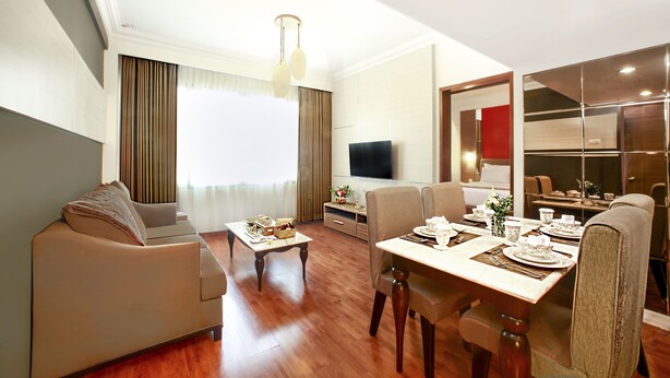 A modern living room with a sofa, dining table set for four, and a flat-screen TV mounted on the wall. - Grand Inna Tunjungan Hotel Surabaya (Surabaya)