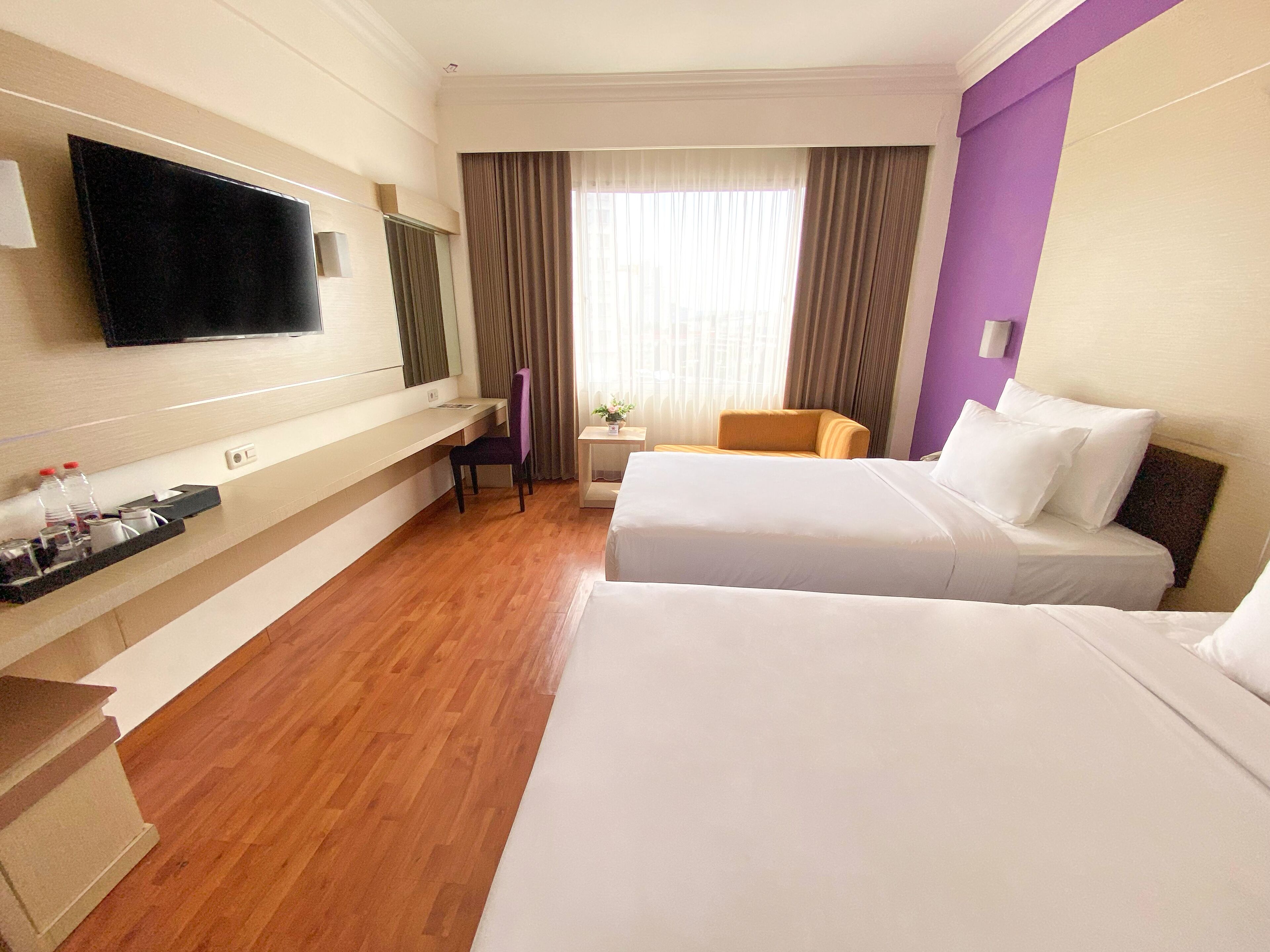 A hotel room with two beds, a TV, a desk with a chair, and a small table with a plant.