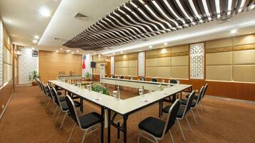 Un salón de conferencias con una larga mesa, sillas y un techo decorativo.
