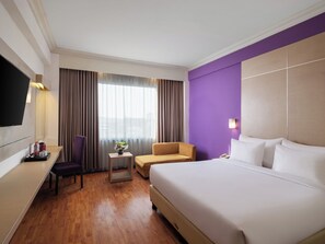 Habitación de hotel con una cama grande, un escritorio con silla, una mesita con un jarrón y un televisor montado en la pared.