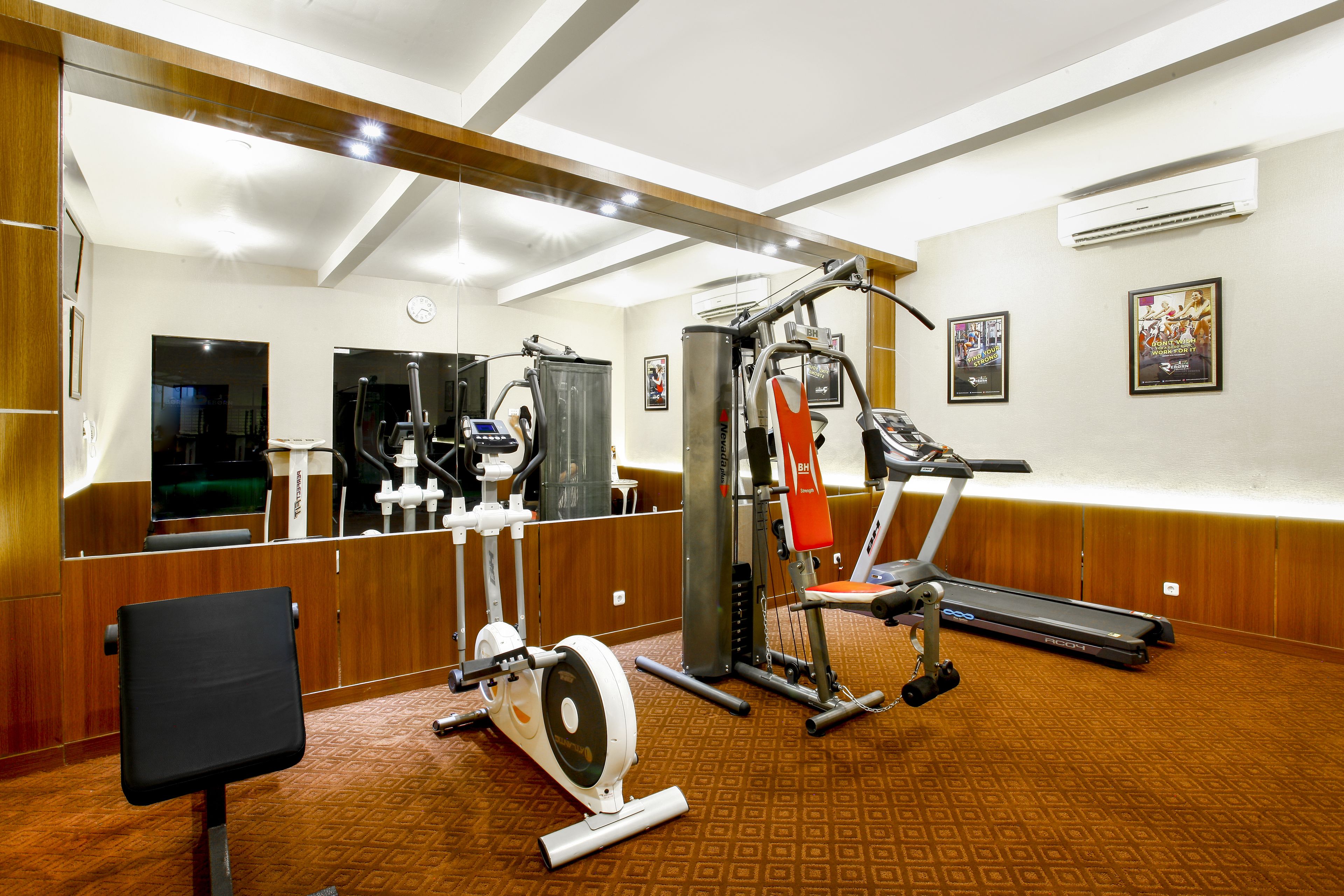 Un gimnasio con equipo de ejercicio, una cinta de correr y un espejo grande.