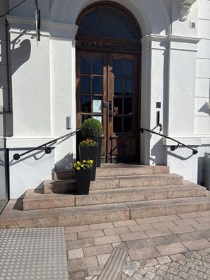 A hotel entrance with a wooden door labeled 'STADSHOTELL,' a small potted plant, and a metal handrail. - Laholms Stadshotell (Laholm)