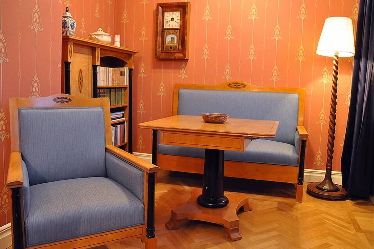 A room with two blue upholstered chairs, a wooden table, a bookshelf, a clock, and a lamp.