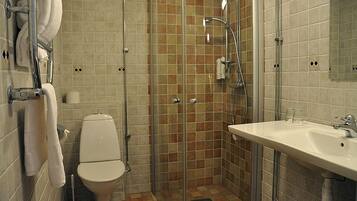 Un baño con inodoro, ducha con puerta de cristal y lavamanos con espejo.