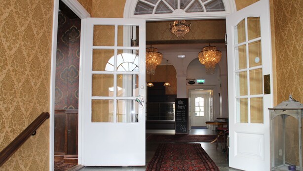 Una entrada imponente con alfombra roja, un candelabro y una escalera de madera.