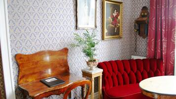 Una habitación con un banco de madera, un sofá rojo, una mesa con una planta y un papel tapiz estampado con cuadros.