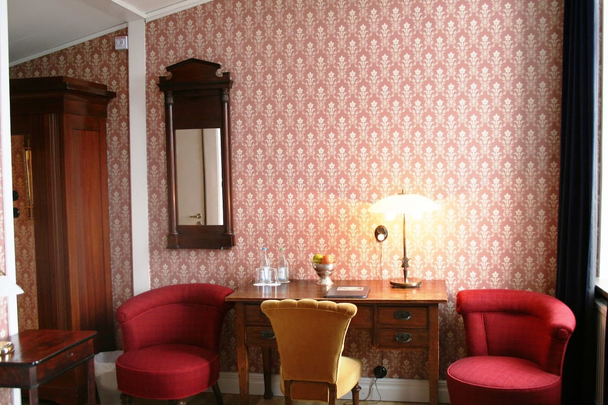 A room with a wooden desk, two red chairs, a yellow chair, a mirror, and a lamp.