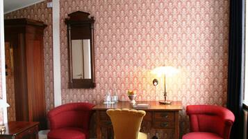 Una habitación con un escritorio de madera, dos sillas rojas, una silla amarilla, un espejo y una lámpara.