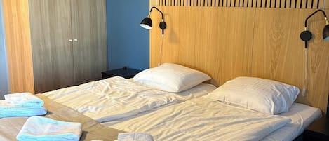 Un dormitorio con cama, dos lámparas de noche, un armario y cabecera con listones verticales.
