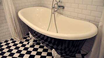 Una vasca da bagno freestanding con piedi a zampa di leone, pavimento a scacchi, pareti rivestite di piastrelle bianche e soffione doccia.