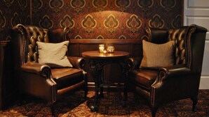 Una habitación con dos sillones de cuero, una mesita redonda con una vela y un papel tapiz estampado.