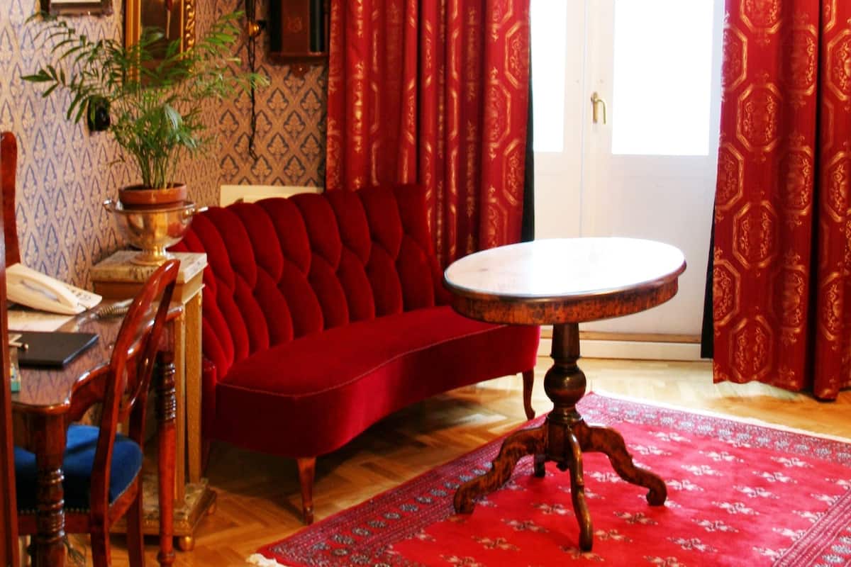A room with a red sofa, a round table, a wooden chair, a potted plant, and a framed picture on the wall.
