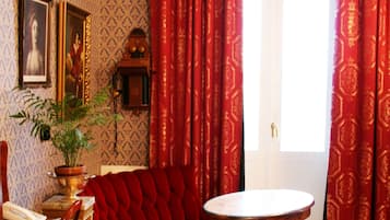 A room with a red sofa, a round table, a wooden chair, a potted plant, and a framed picture on the wall.