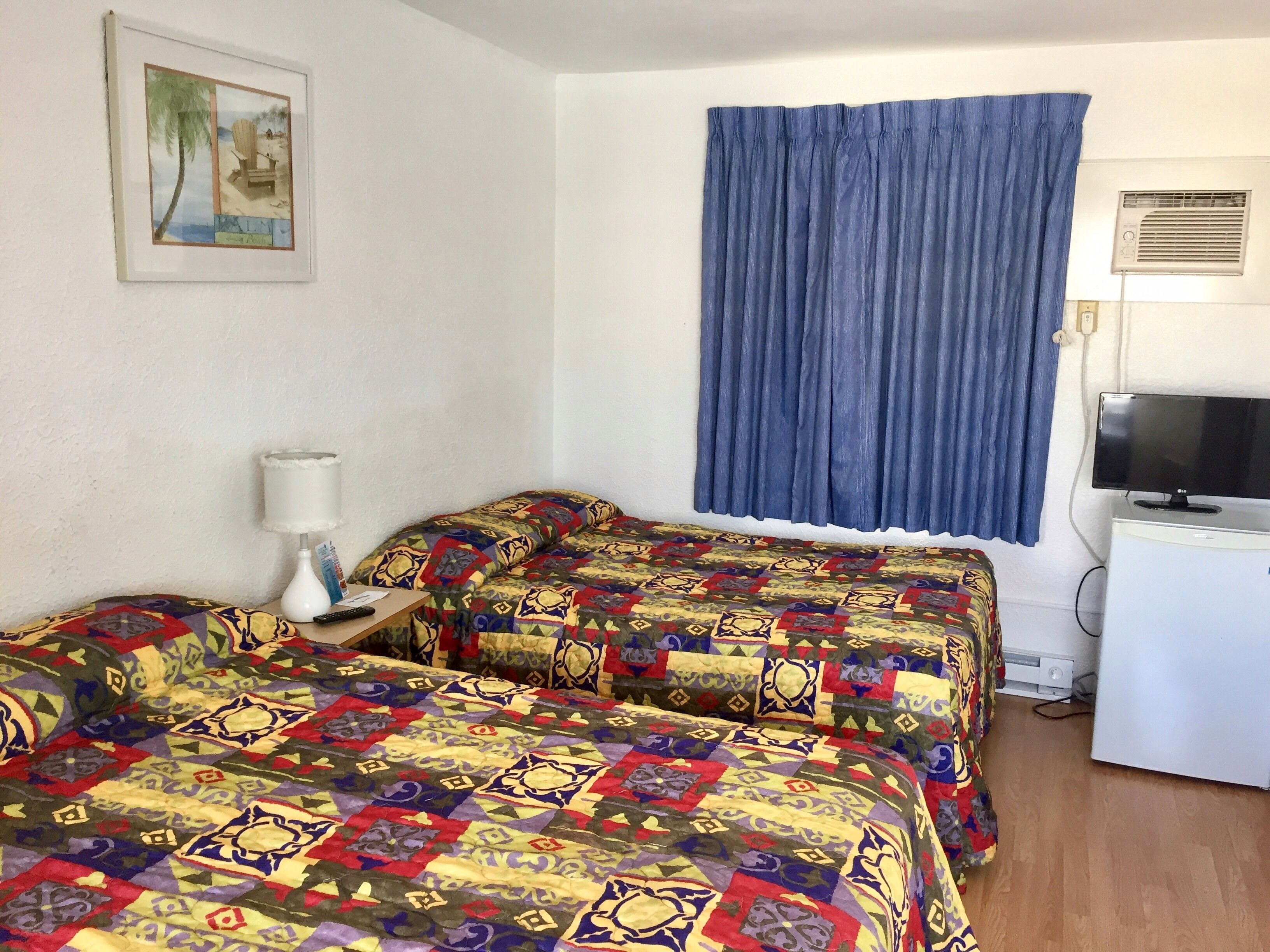 A room with two beds, a television, and a window with blue curtains.